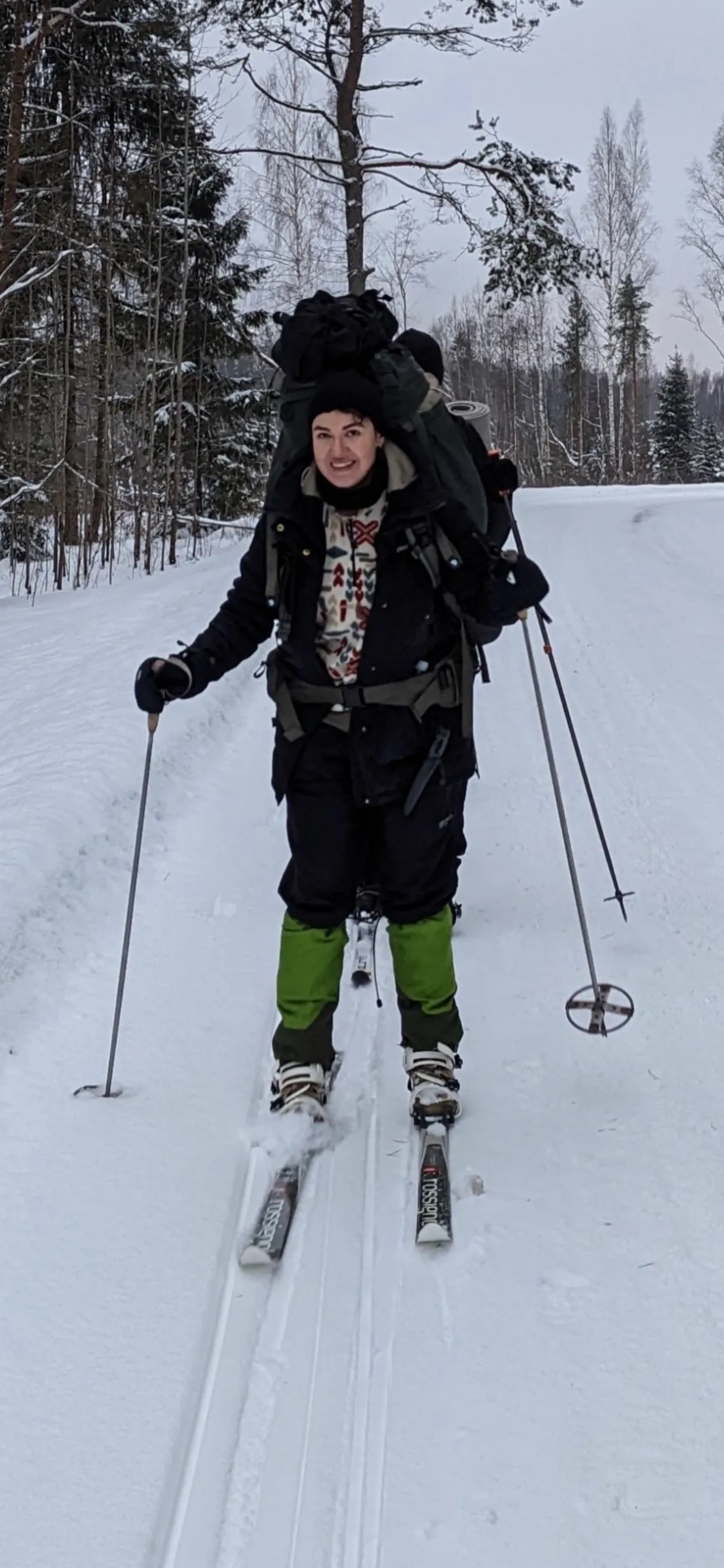 Stella on cross-country skis on a snowy road, wearing a large backpack and holding ski poles.
